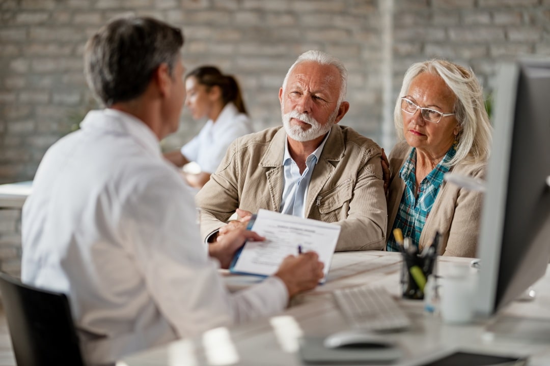 Medicare open enrollment represented by picture of a Mature couple planning their health insurance policy with a doctor at clinic.