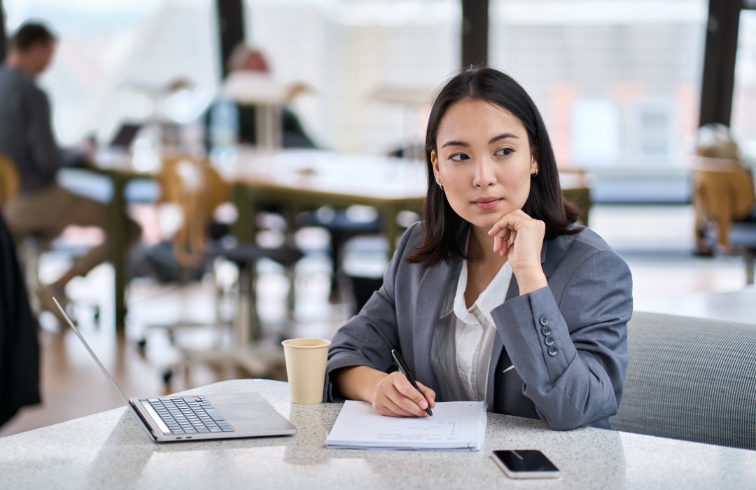 Young Asian business woman working in modern office, taking notes and thinking, representing financial decisions when getting a divorce.